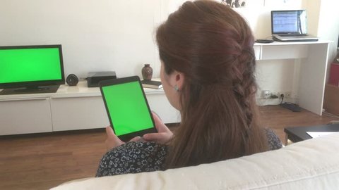 Girl Watching Tablet TV Green Screen, Dolly Shot. Charming young woman watching green screened television and tablet at home. Ungraded 4k