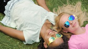 Ladies in sunglasses enjoying summer, lying on grass, surfing web on smartphone