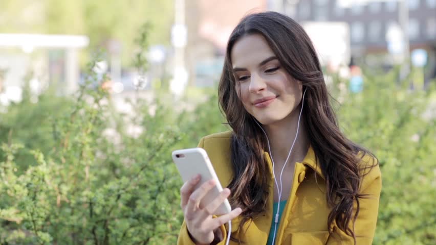 technology, lifestyle and people concept - smiling young woman or teenage girl with smartphone and headphones listening to music and drinking coffee on city street