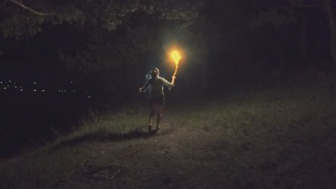 Brave girl traveling the night forest holding a fiery torch in hand. Slow motion.