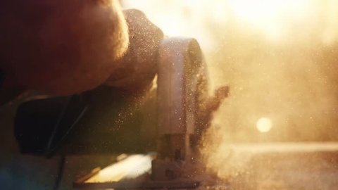 Man is craft working at a work bench with power tools in slowmotion during sunset with beautiful lens flare. 1920x1080