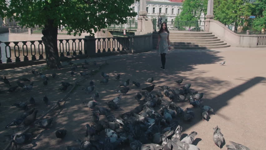 Young woman happily running on a flock of pigeons, which rises in the air in slow motion.