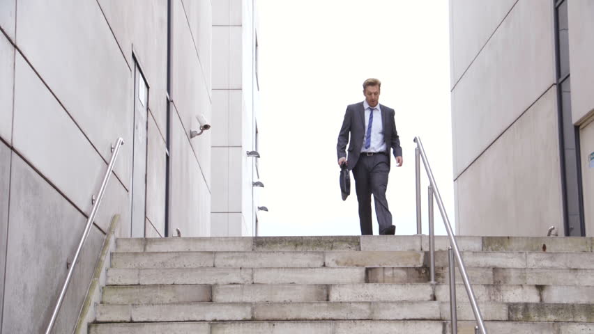 Businessman late for work in the city. He is wearing a suit and carrying a briefcase. He runs down some stairs and out of the frame. Royalty-Free Stock Footage #19064875