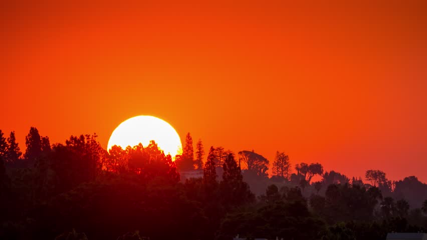 Sunrise sun in fiery orange sky rising above Hollywood Hills in Los Angeles, California, 4K UHD timelapse.