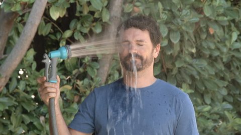 Slow motion of model released man spraying himself in the face with a hose outside on a hot summer's day.