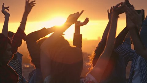 Group of young multi-ethnic people having fun dancing with raised arms to the music played by dj at rooftop party at sunset
