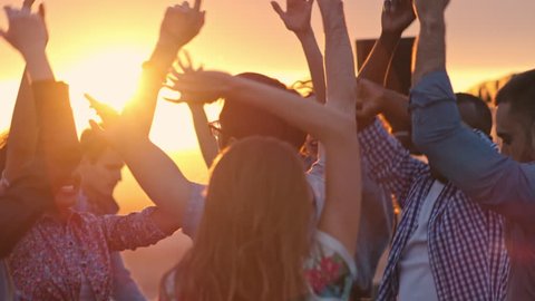 Group of young multi-ethnic people dancing with raised arms to the music played by dj at rooftop party at sunset