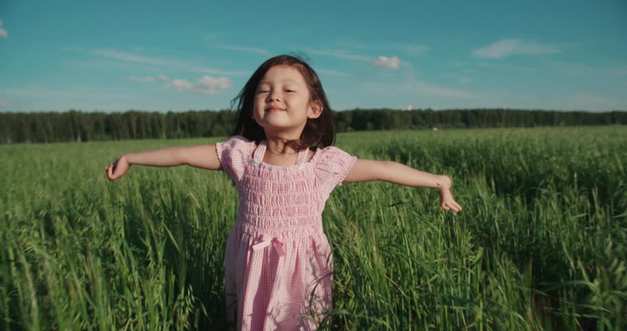 Little Asian girl running in a green field of young wheat,slow motion