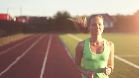 Slow motion. Hot air evoporates. Beautiful young woman exercise jogging and running on athletic track on stadium at sunrise. Cinematic style video.