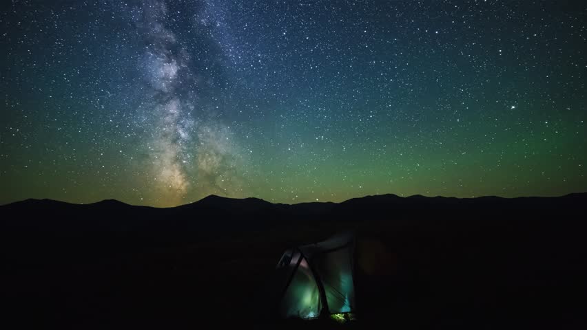 The Milky Way galaxy moving over mountains with camp tent on a foreground