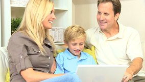 Little blonde boy using a laptop & watched by proud parents