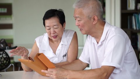 Asian senior elder couple reading news together from tablet in small library. Learning and study concept