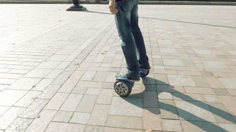 Man is riding hoverboard or electric self balancing gyro scooter board on the side walk. Modern and trendy urban transportation gadget. Popular city futuristic device among young people.