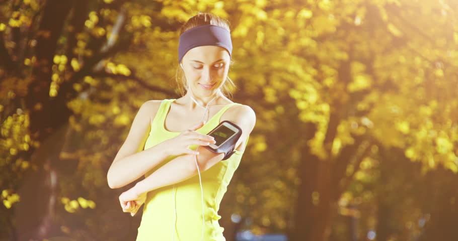 Runner woman with Smartphone running in park Exercising outdoors. 4K DCi SLOW MOTION 120 fps. Athletic Sportswoman checking on Fitness app, Turning on Music, Using Cellphone. Lens fl.