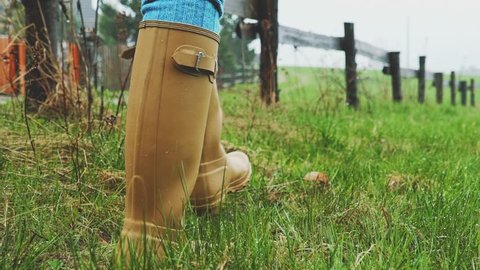 Yellow Rain Boots Walking on a Wet Grass under the Rain. SLOW MOTION 120 fps. Woman walking in the field under the pouring rain, Close Up on Gumboots. Autumn or Spring rainy day.
