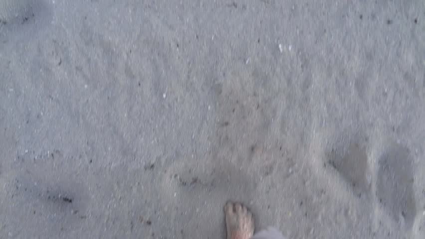 Man walking barefoot in the sand of a beach. 