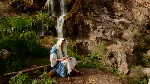 the Artist in the Traditional Hebrew Dress Sitting Near the Waterfall. a Man Holding a Paper and Sketch Drawing. View of a Small Waterfall in Jordan.