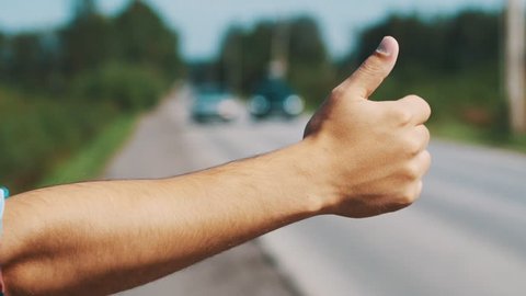 Man stay at road with thumb up in summer sunny day. Hitchhiking. Traveler. Transportation