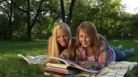 Happy Teenage girls reading a book outdoors. Teenage girlfriends having fun and laughing. Slow motion video footage 1080 full hd. High speed camera shot