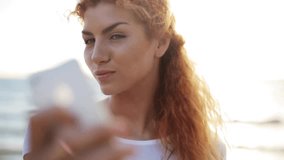 people, technology and leisure concept - happy young redhead woman taking selfie with smartphone on beach