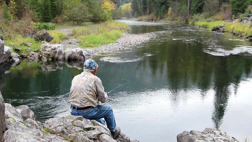 Old man fishing on a river in a lush forest Montana