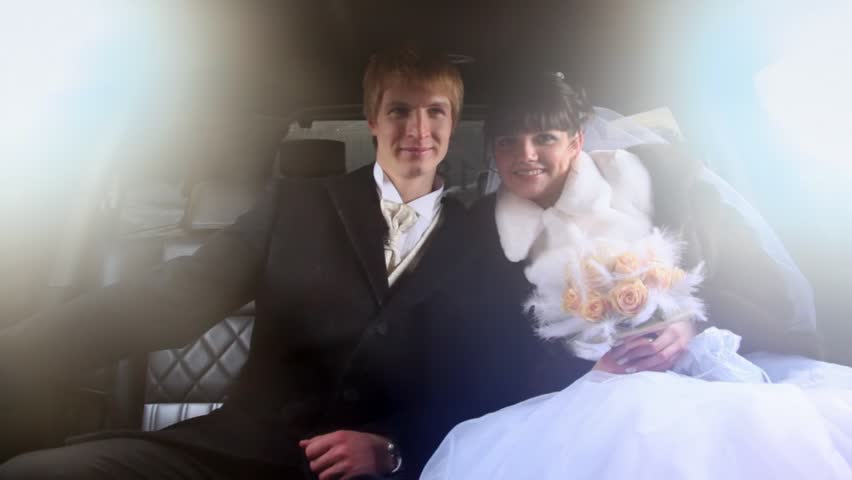 Newly-married couple sits together in limousine and kisses