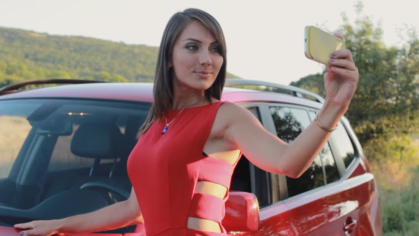 Attractive young woman taking selfie on the phone near her car