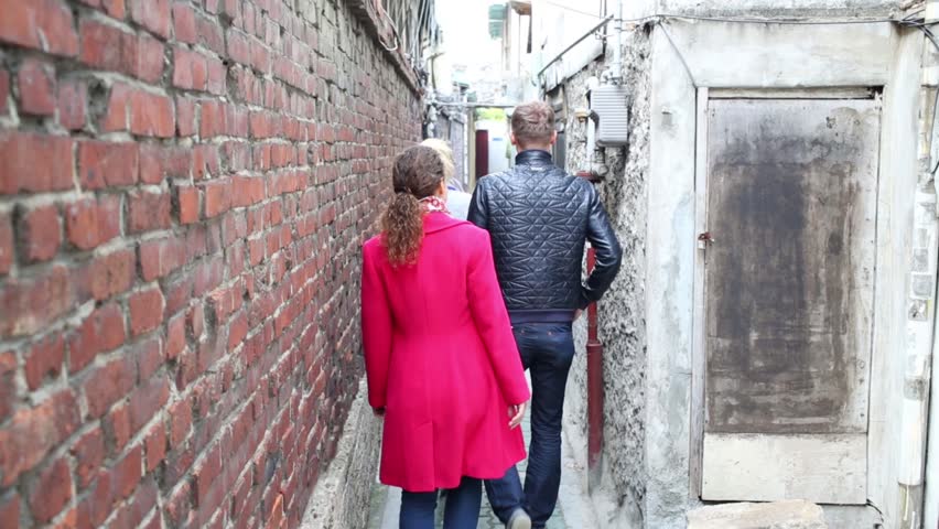 Man and two women going in narrow passing with brick wall at street in Seoul.