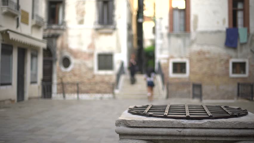 Venetian old well with a woman walking near that.