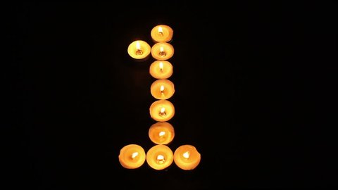 Static shot of burning tealight candles arranged like pixel art numeral digits to represent the number one on a black background.