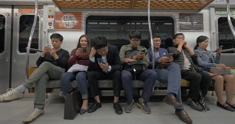 SEOUL, SOUTH KOREA - OCTOBER 22, 2015: Group of male and female commuters sitting in subway train and using smart phones to entertain themselves during the ride