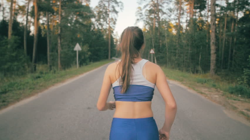 Athletic youg woman Jogging in a park. Slow motion. Steadycam shot.