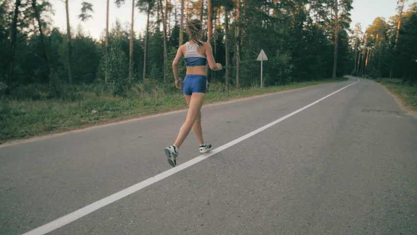 Athletic youg woman Jogging in a park. Slow motion. Steadycam shot.