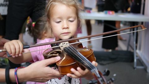SOFIA, BULGARIA - AUG 28, 2016: Free public cultural urban festival in pedestrian city center. Child little girl try play violin - music instrument educative demonstration 