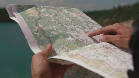 Man's hand drawing on map by finger, checking way when looking to lake ahead