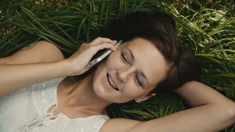 beautiful woman lying on the grass talking on the phone and smiling