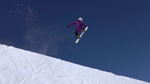 SLOW MOTION: Young pro snowboarder riding the half pipe in big mountain snow park, jumping high out of the halfpipe wall, performing tricks and rotations with grabs in sunny winter