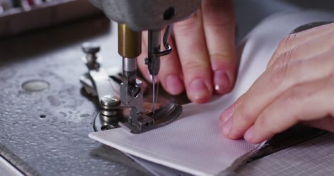 Super slow motion of a professional sewing machine stitching with white thread an Italian  couture fabric, The seamstress sews a high fashion outfit. concept of industry, tradition, fashion
