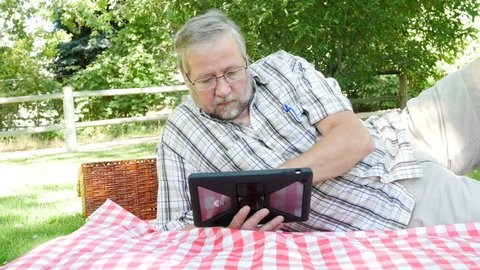 An older man using his ipad at a park