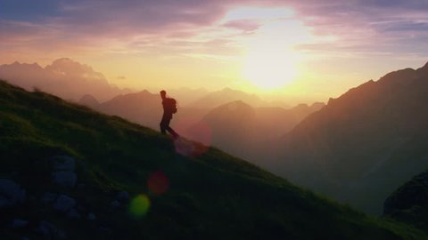 Aerial - Epic shot of a man hiking on the edge of the mountain as a silhouette in colorful sunset (edited version)