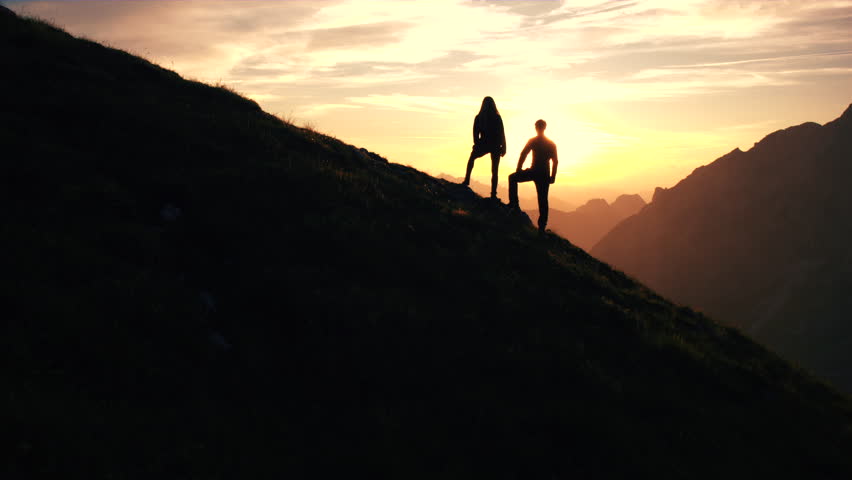 Aerial, edited - Silhouette of a couple giving each other a high five celebrating successful climb on the mountain in beautiful sunset Royalty-Free Stock Footage #19249195