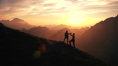 Aerial, edited - Silhouette of a couple giving each other a high five celebrating successful climb on the mountain in beautiful sunset