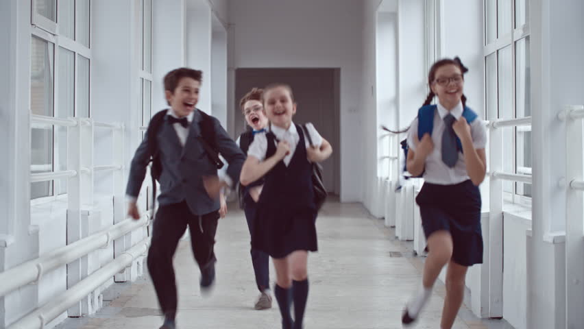 Lockdown of four excited laughing schoolgirls and schoolboys wearing uniform and backpacks jumping up and running along school hallway towards camera | Shutterstock HD Video #19250860