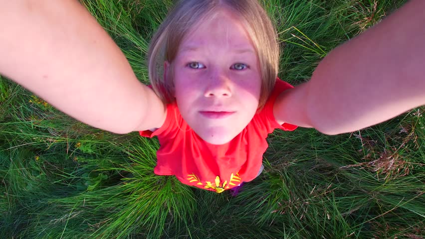 Little blond girl playing with a drone. Girl having fun falls on the grass, letting go a toy 