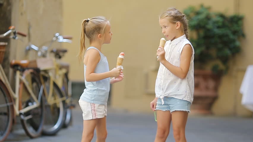 Adorable little girls eating ice-cream outdoors at summer. Cute kids enjoying real italian gelato near Gelateria in Rome