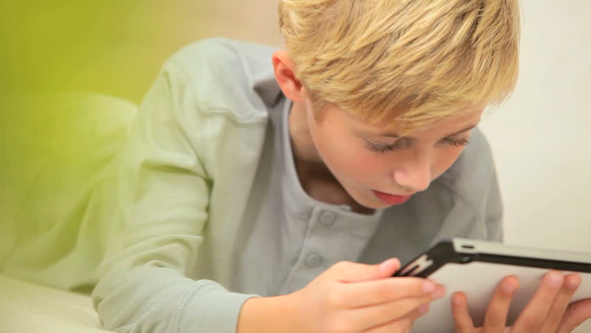 Young caucasian boy lying on home sofa using a modern wireless tablet