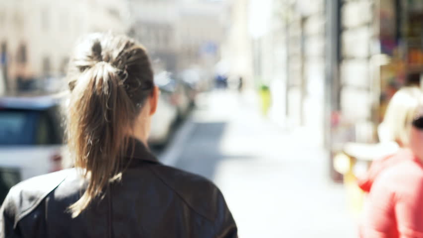 Portrait of pretty, happy woman walking in city during sunny day 
