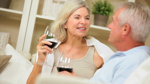 Senior couple in close up drinking wine and laughing on their home sofa