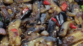 Baked eggplant with onions, garlic, red hot chili pepper and walnuts on the black plate, close up