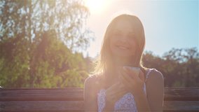 High quality 10bit footage of Happy smiling girl using a smart phone in a city park at sunset. Made from 14bit RAW.